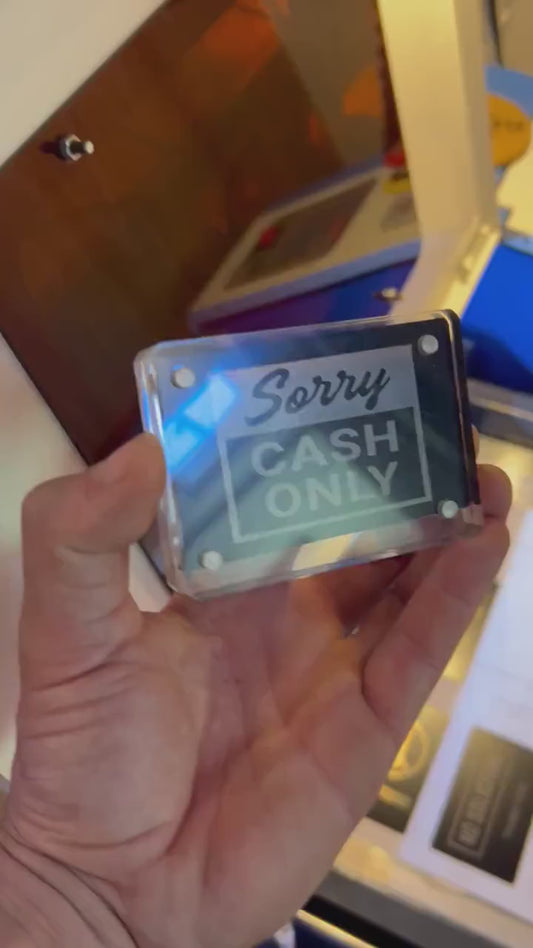 Hand holding a laser engraved black/silver Sorry Cash Only retail signage placard, shown in optional acrylic display case
