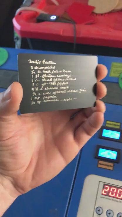 Hand holding a laser engraved metal handwriting engraving on a matte black/silver metal keepsake wallet card
