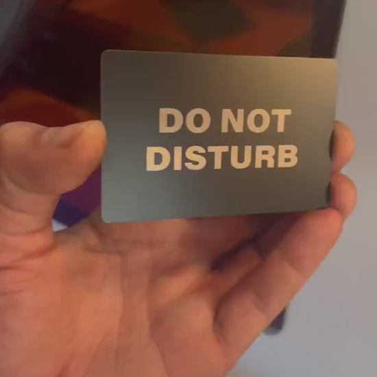 Hand holding laser engraved metal placard that reads: "Do Not Disturb" in black/silver