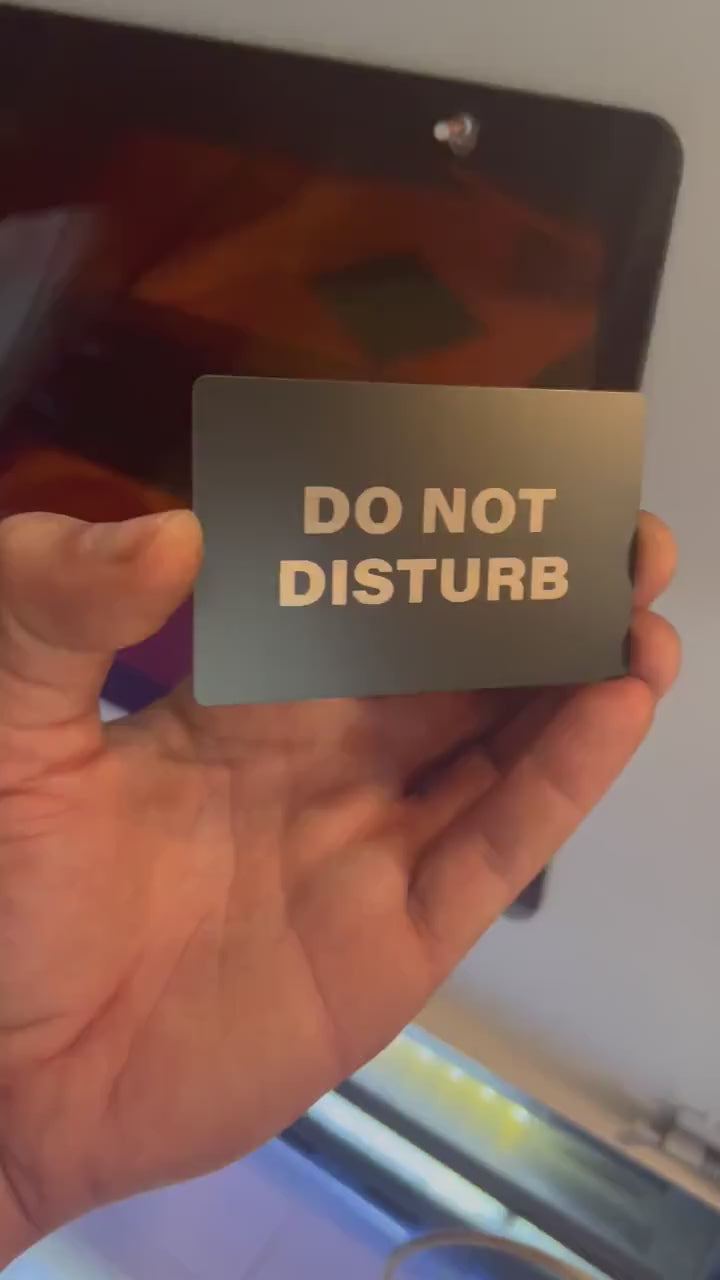 Hand holding laser engraved metal placard that reads: "Do Not Disturb" in black/silver