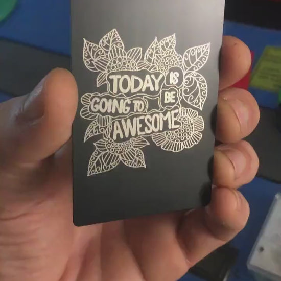 Angled shot of custom black/silver engraved metal keepsake card with motivational text and flower artwork