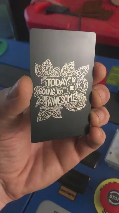 Angled shot of custom black/silver engraved metal keepsake card with motivational text and flower artwork