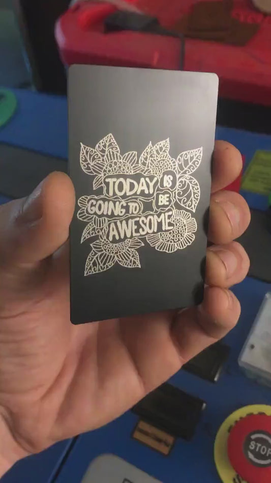 Angled shot of custom black/silver engraved metal keepsake card with motivational text and flower artwork