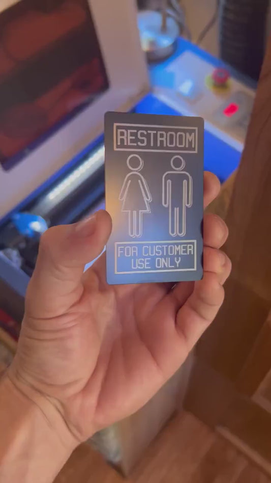 Close up video of hand holding a laser engraved metal retail signage placard, with Restroom and "For Customer Use Only" design