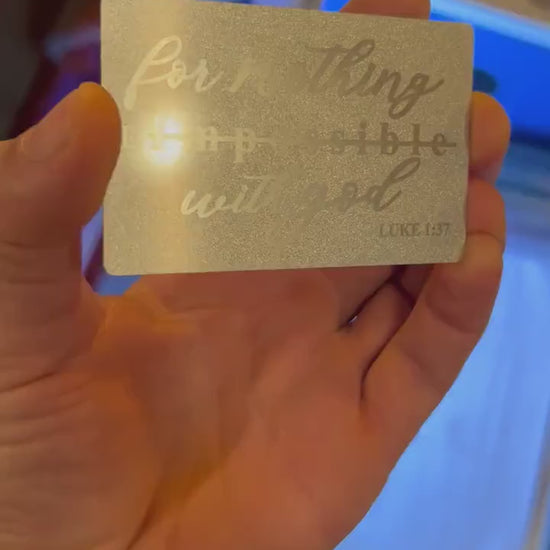 Video of engraved metal wallet card turning under light to show reflective finish with bible reference text