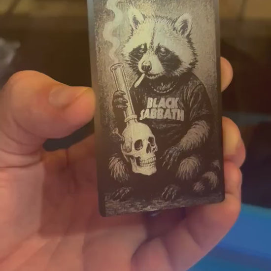 Hand holding a laser engraved metal/black illustrated cute animal gift card, with heavy metal raccoon design