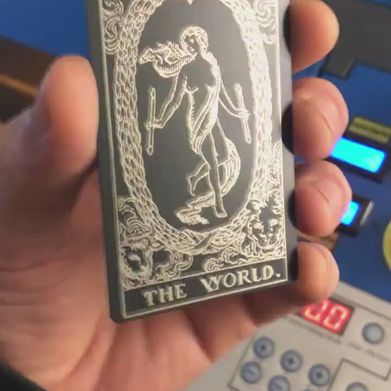 Hand holding a laser engraved black/silver the world metal tarot card