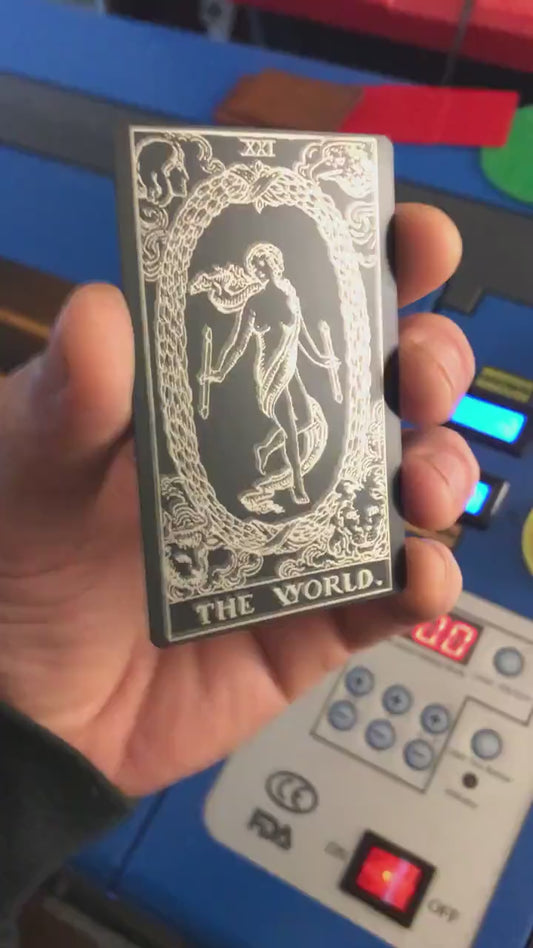 Hand holding a laser engraved black/silver the world metal tarot card