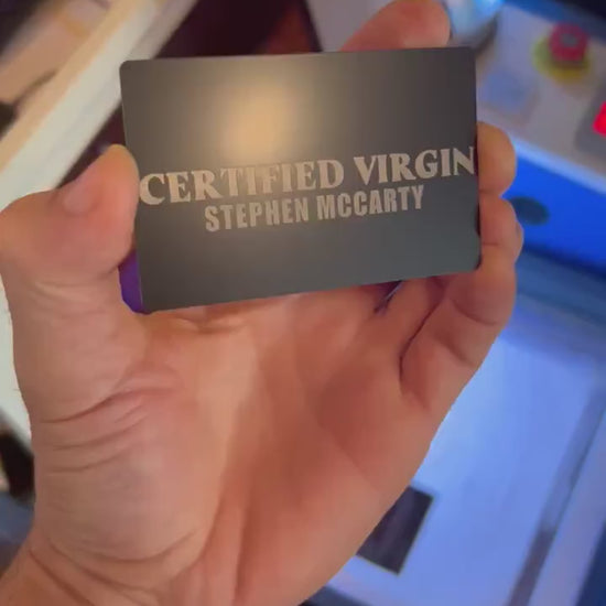 Close up video of hand holding a laser engraved metal gag gift card with "CERTIFIED VIRGIN" text, with a custom personalized name beneath in black/silver