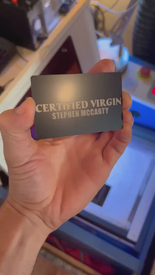 Close up video of hand holding a laser engraved metal gag gift card with "CERTIFIED VIRGIN" text, with a custom personalized name beneath in black/silver