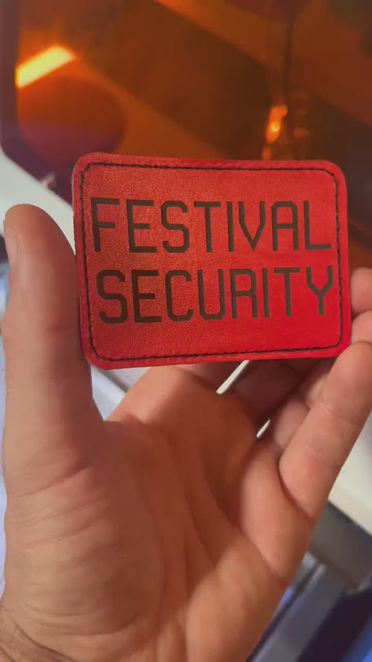 Hand holding a laser engraved red 3.5x2.5" Festival Security patch with heat activated adhesive backing in front of a laser engraving machine