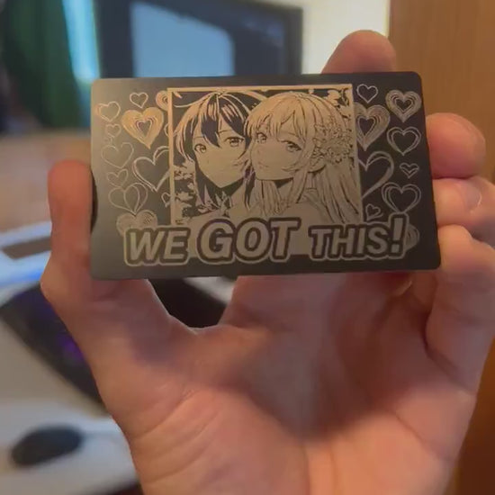 Metal laser engraved keepsake card with We Got This text and two anime line art drawing girls and heart patterns in black/silver anodized aluminum