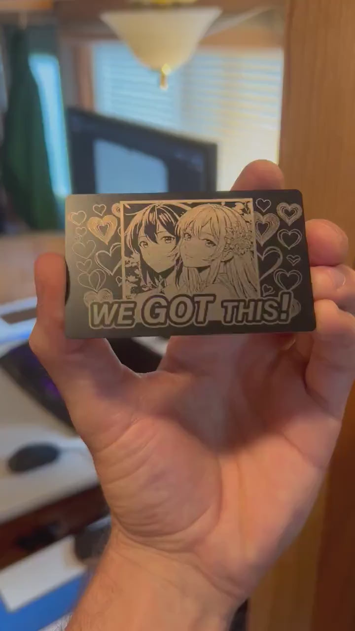 Metal laser engraved keepsake card with We Got This text and two anime line art drawing girls and heart patterns in black/silver anodized aluminum