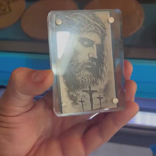 Close up video of hand holding a laser engraved metal keepsake gift card with Crown of Thorns Jesus Christ Crucifix illustration artwork engraving, shown in optional acrylic display case