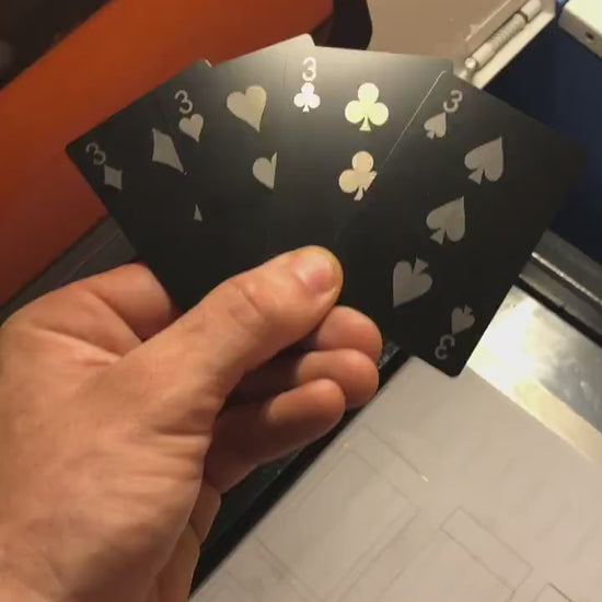 Close up video of hand holding 4 laser engraved metal playing cards with 3 of diamonds, 3 of hearts, three of clubs and three of spades cards