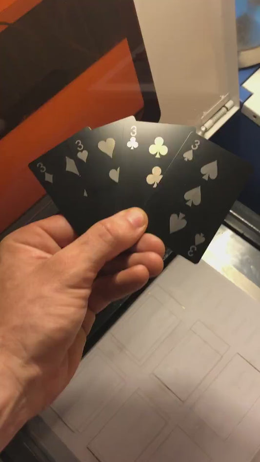Close up video of hand holding 4 laser engraved metal playing cards with 3 of diamonds, 3 of hearts, three of clubs and three of spades cards