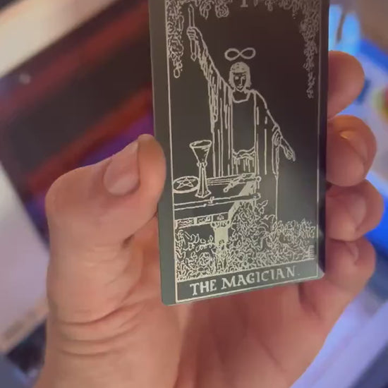 hand holding laser engraved The Magician metal tarot card in matte black/silver