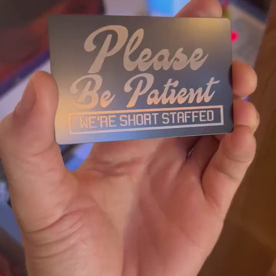 Close up video of hand holding a laser engraved metal retail signage placard with Please Be Patient, We're Short Staffed modern text 