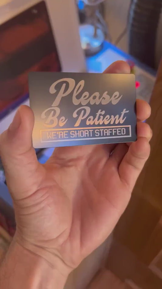 Close up video of hand holding a laser engraved metal retail signage placard with Please Be Patient, We're Short Staffed modern text 