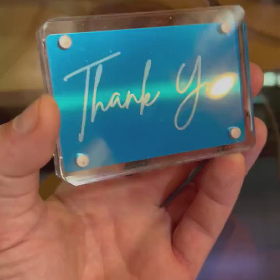 Hand holding a laser engraved blue/silver metal Thank You keepsake card, shown in optional Acrylic display case