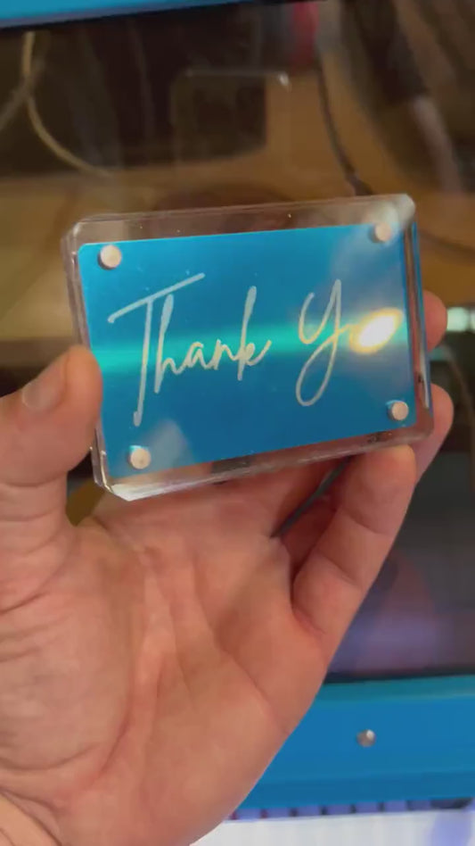 Hand holding a laser engraved blue/silver metal Thank You keepsake card, shown in optional Acrylic display case
