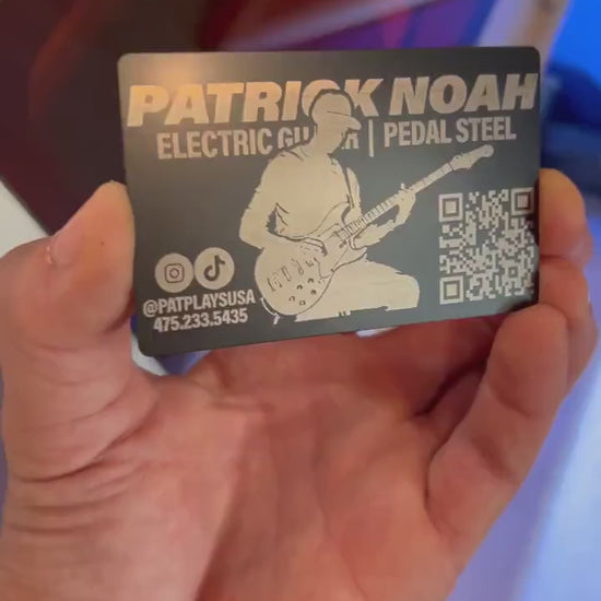 Hand demonstrating a metal laser engraved metal promotional business card, with personalized guitarist design in front of a laser engraving machine