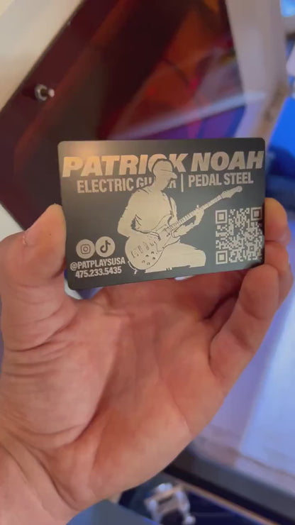 Hand demonstrating a metal laser engraved metal promotional business card, with personalized guitarist design in front of a laser engraving machine