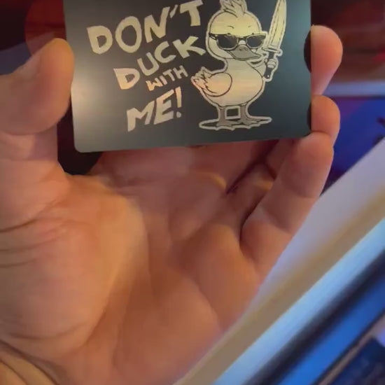 Hand holding a laser engraved black/silver metal gag gift card with cute duckling and "DON'T DUCK WITH ME" typography text