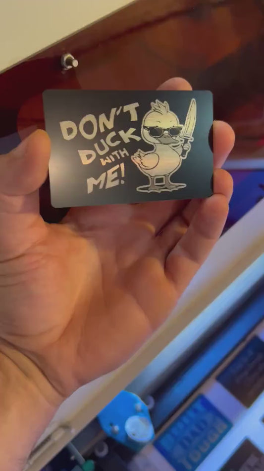 Hand holding a laser engraved black/silver metal gag gift card with cute duckling and "DON'T DUCK WITH ME" typography text