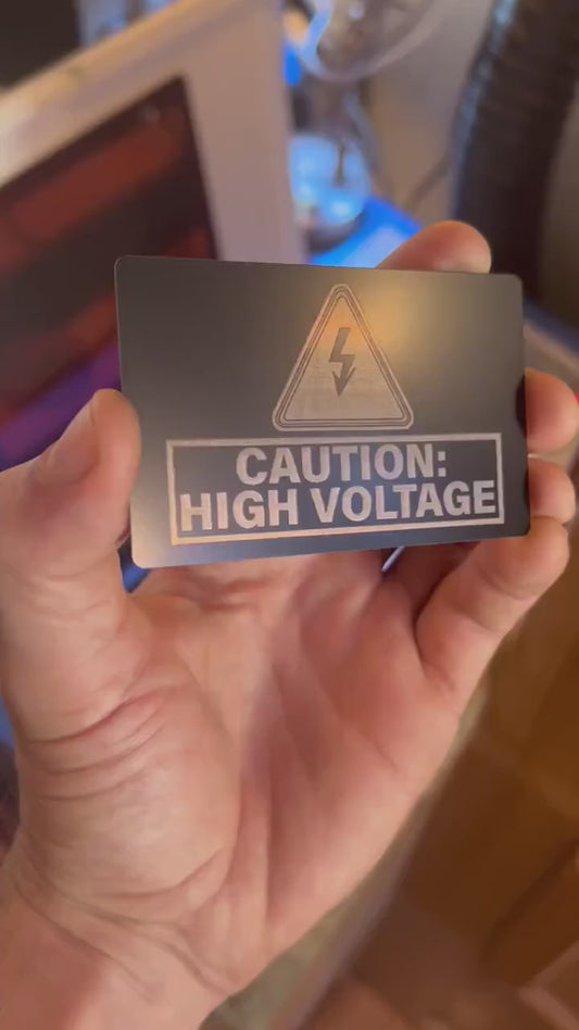 Close up video of hand holding a laser engraved metal safety warning signage, with Caution High Voltage and an electrical symbol