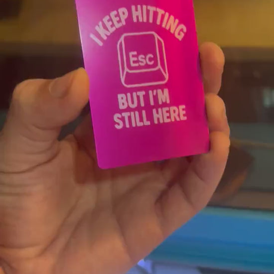 Hand holding a laser engraved purple and silver anodized aluminum I Keep Hitting Esc But I'm Still Here card