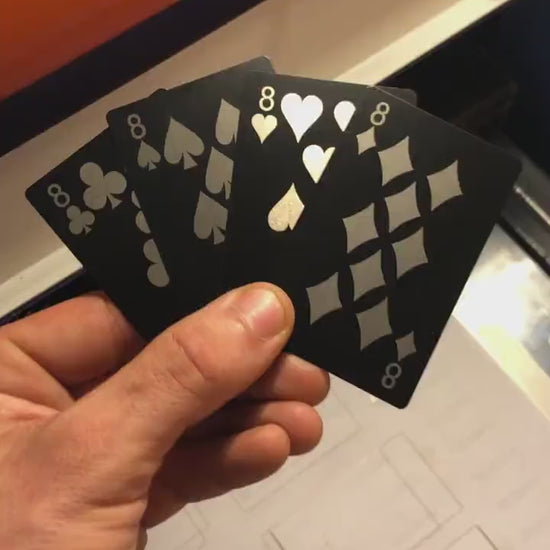 Close up video of hand holding 4 laser engraved metal poker cards with 9 of clubs, 8 of spades, eight of hearts, eight of diamonds cards