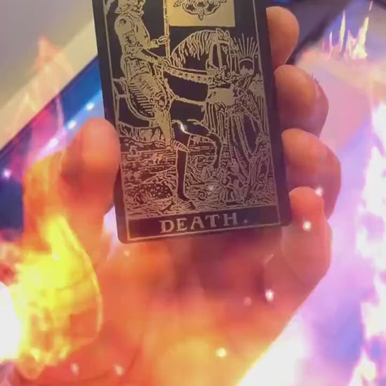 Hand holding a laser engraved black/silver metal "Death" tarot card laser engraving, with a fiery special effects graphic