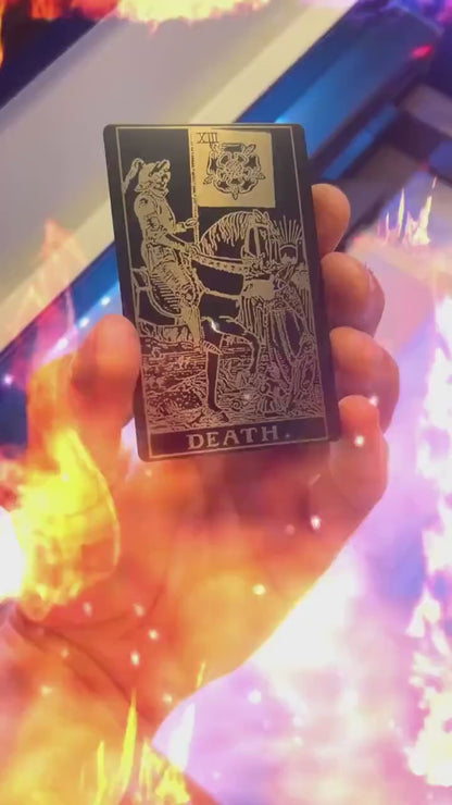 Hand holding a laser engraved black/silver metal "Death" tarot card laser engraving, with a fiery special effects graphic