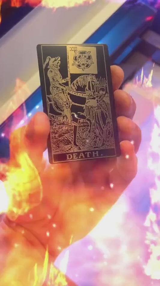 Hand holding a laser engraved black/silver metal "Death" tarot card laser engraving, with a fiery special effects graphic