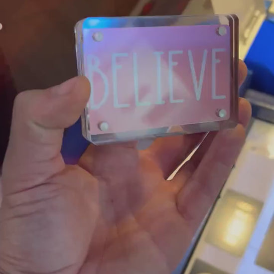 Human hand showcasing rose gold metal gift card engraved with motivational “BELIEVE” word design