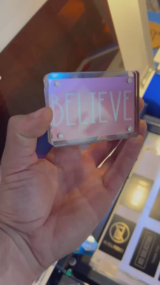 Human hand showcasing rose gold metal gift card engraved with motivational “BELIEVE” word design
