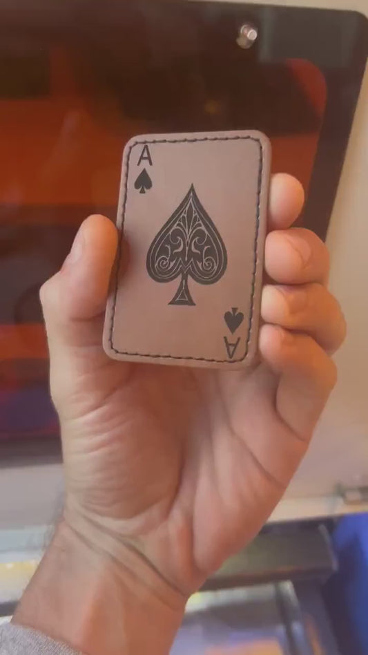 Hand holding a laser engraved brown leather ace of spades patch, rotating to demonstrate leather burning