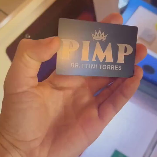Hand holding a laser engraved metal keepsake card with Pimp and personalized name engraving in front of a laser engraving machine