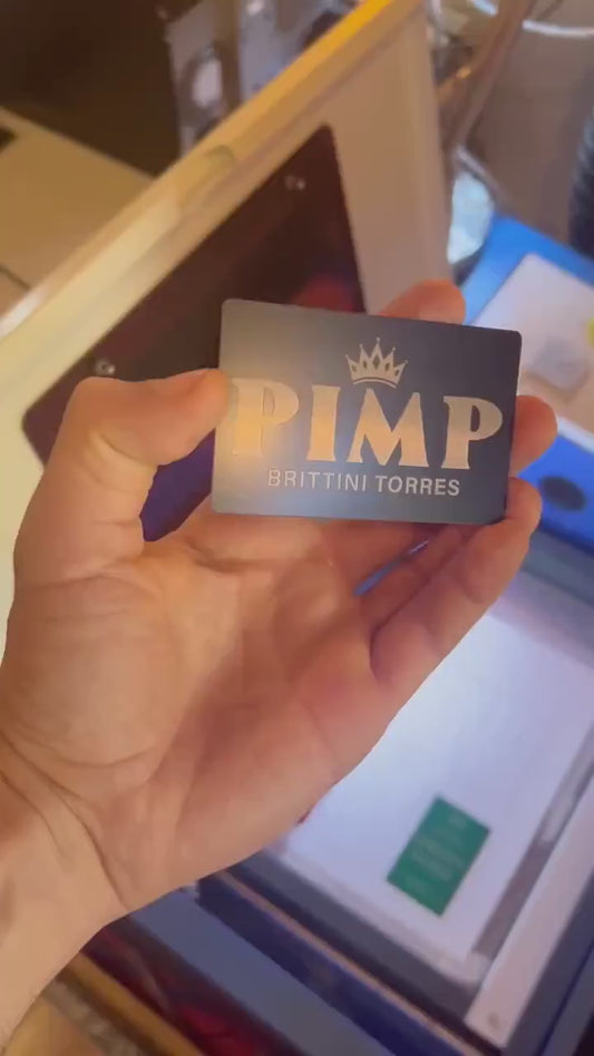 Hand holding a laser engraved metal keepsake card with Pimp and personalized name engraving in front of a laser engraving machine
