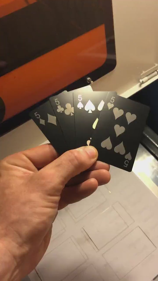 Hand holding a laser engraved black/silver metal playing cards Five of Diamonds, Five of Clubs, Five of Spades & Five of Hearts