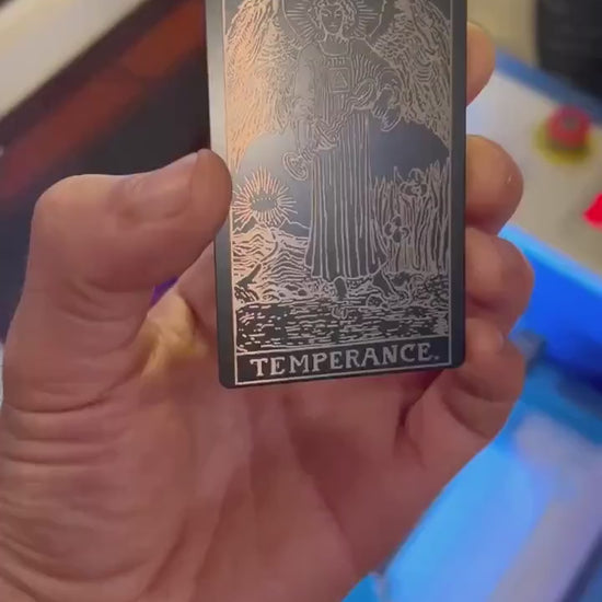 Video of hand demonstrating a black/silver metal Temperance tarot card design under lighting showing how reflective the metal is