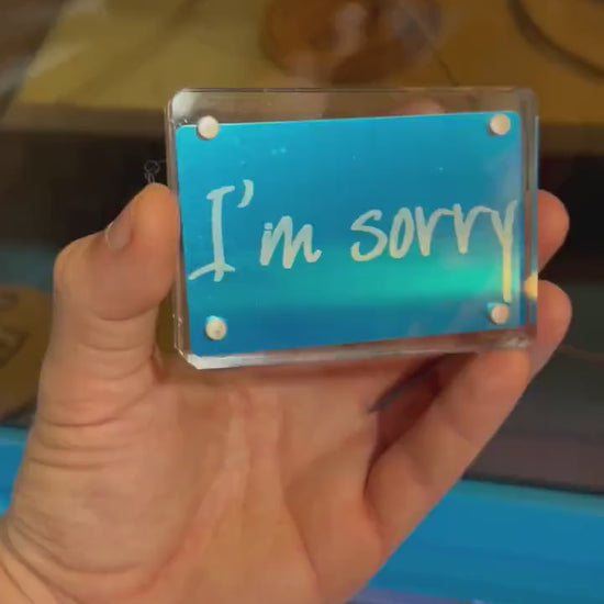 Hand holding a laser engraved blue/silver I'm Sorry keepsake greeting card, displayed in optional acrylic display case