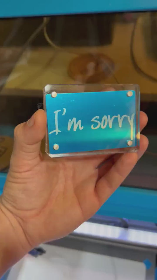Hand holding a laser engraved blue/silver I'm Sorry keepsake greeting card, displayed in optional acrylic display case