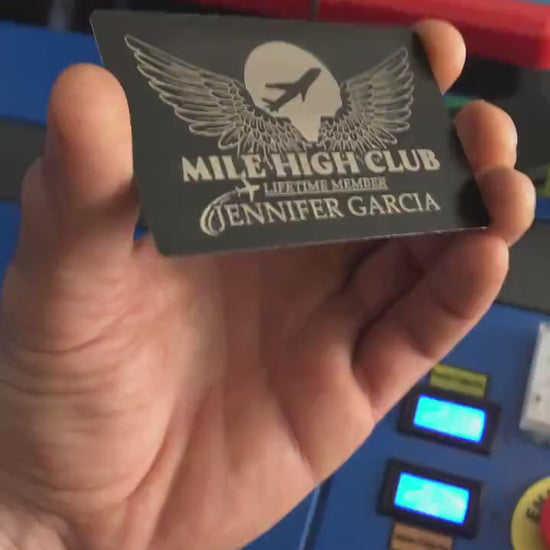 Close up video of hand holding a laser engraved metal keepsake funny gift card with Mile High Club: Lifetime Member and customer supplied personalized name engraving below in black/silver