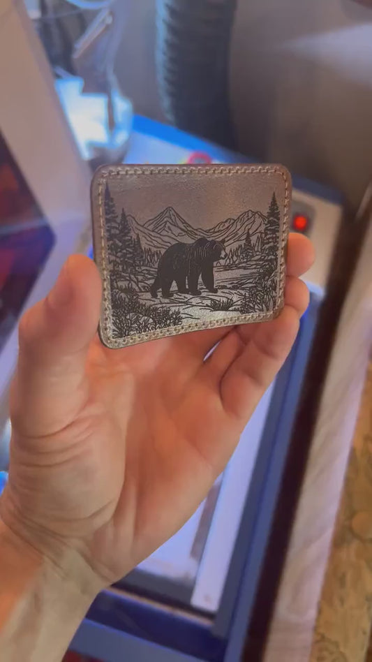 Hand holding a laser engraved dark brown leather patch with brown bear and mountain scenery leather burned design and heat activated adhesive backing