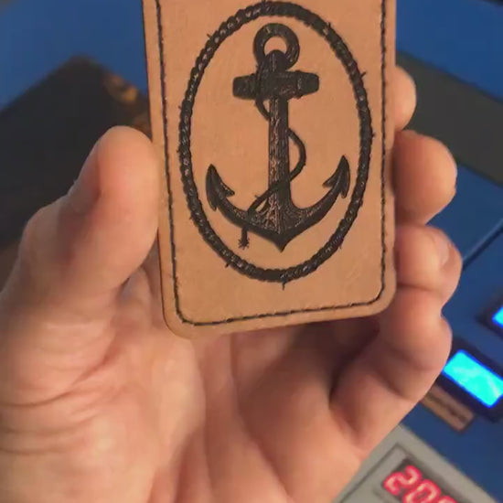 Close up video of hand holding a leather engraved Anchor and rope knot graphic patch