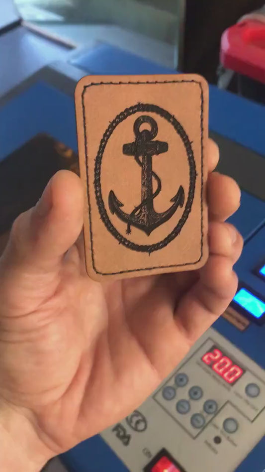 Close up video of hand holding a leather engraved Anchor and rope knot graphic patch