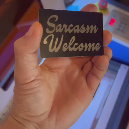 Close up video of hand holding a laser engraved metal keepsake card with "Sarcasm Welcome" cursive typography text
