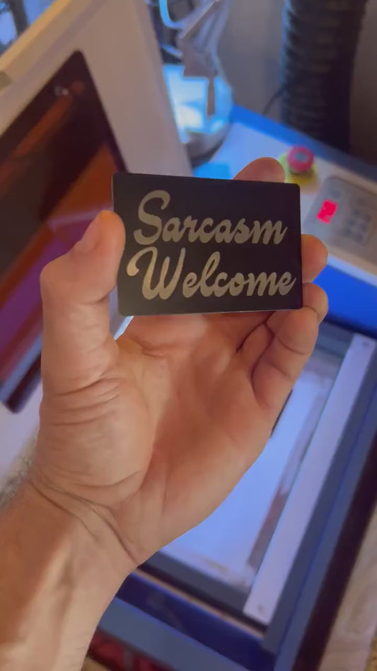 Close up video of hand holding a laser engraved metal keepsake card with "Sarcasm Welcome" cursive typography text